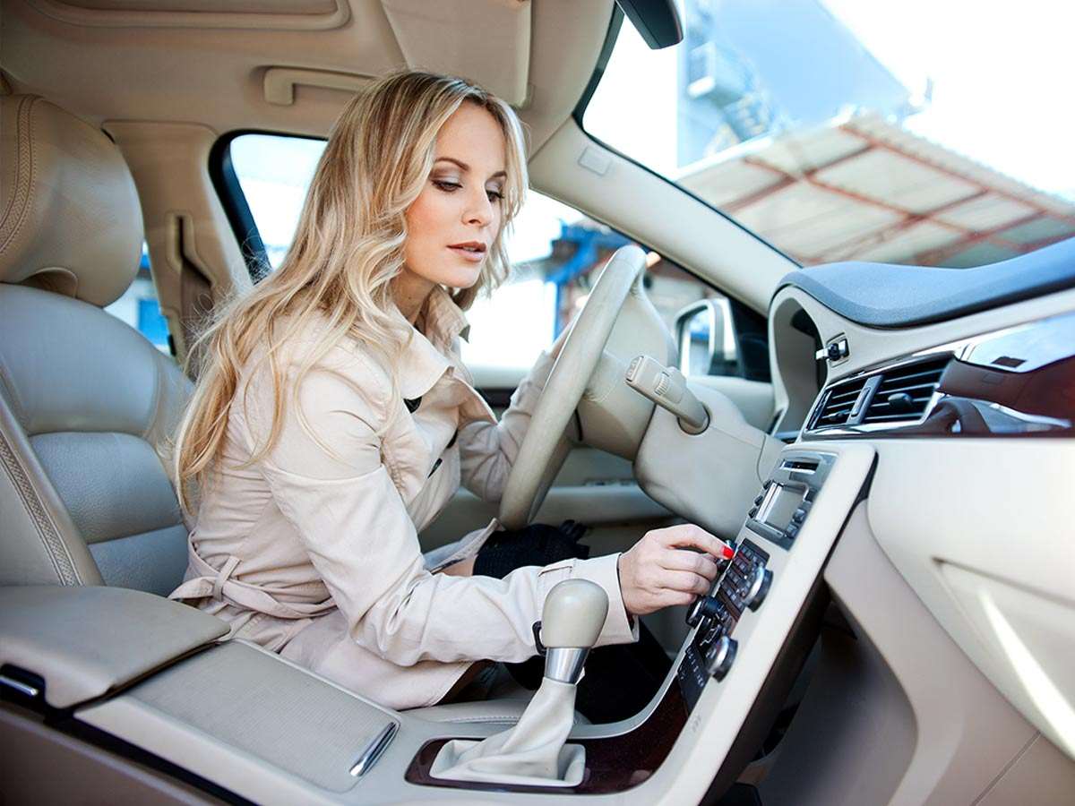 A woman driving her car adjusts the volume on the audio system.